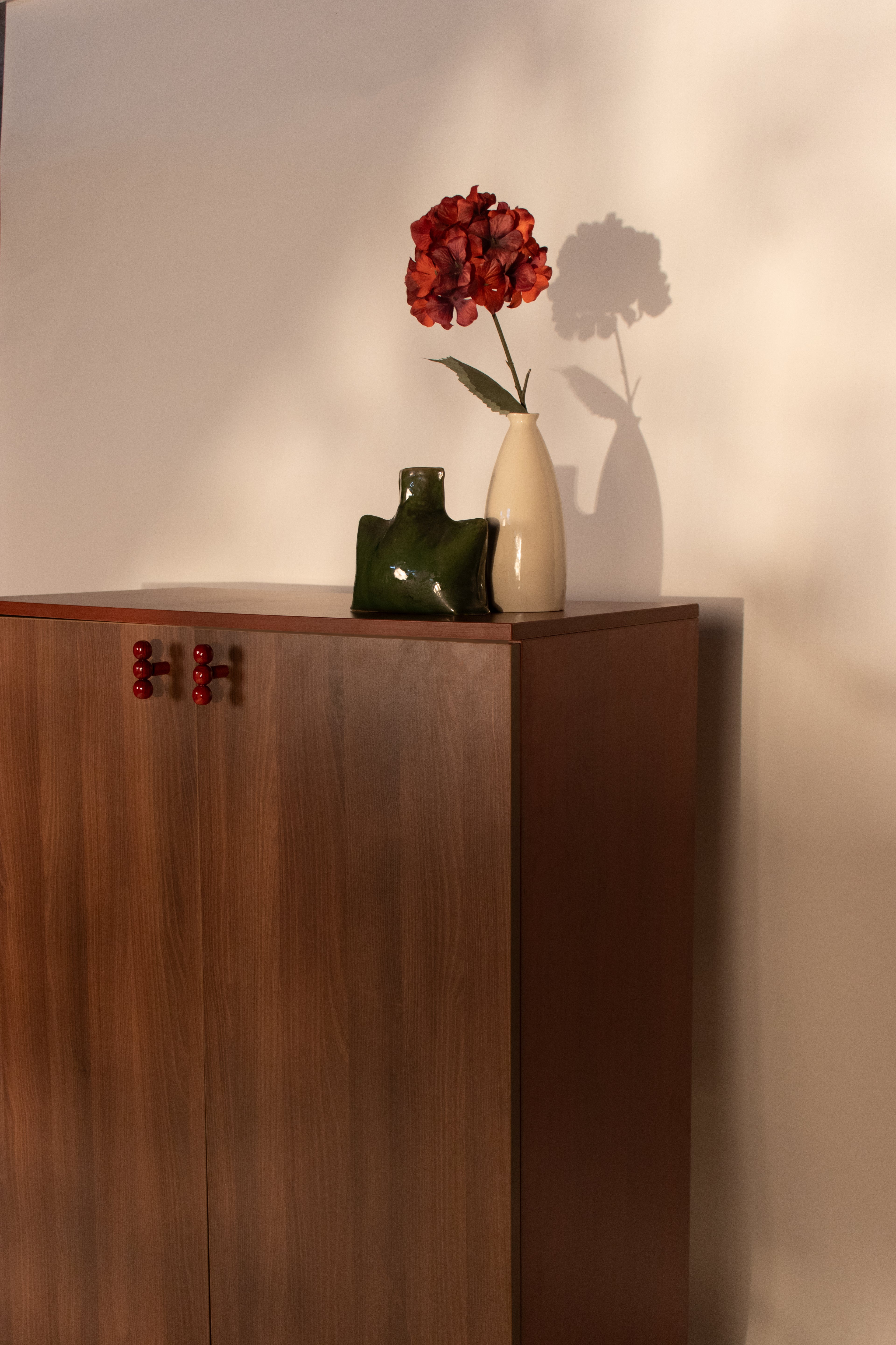 Wooden sideboard with red knob handles shown from side angle with vase styling by RISA